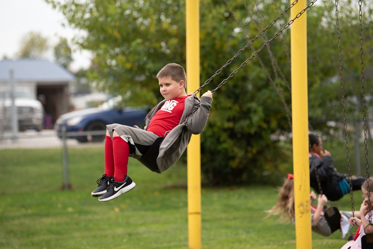 elementary school student playing on the playground swings